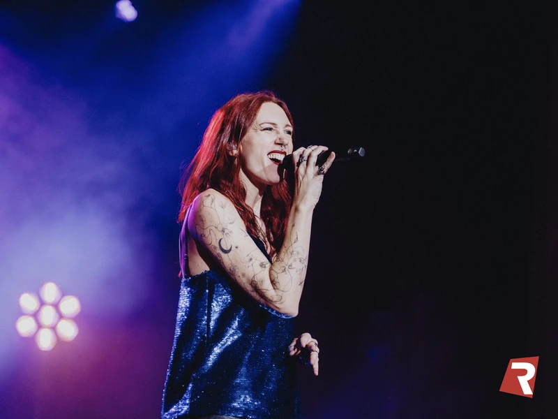 Lollirox chante sur scène, top à paillettes bleues, sous les lumières violettes