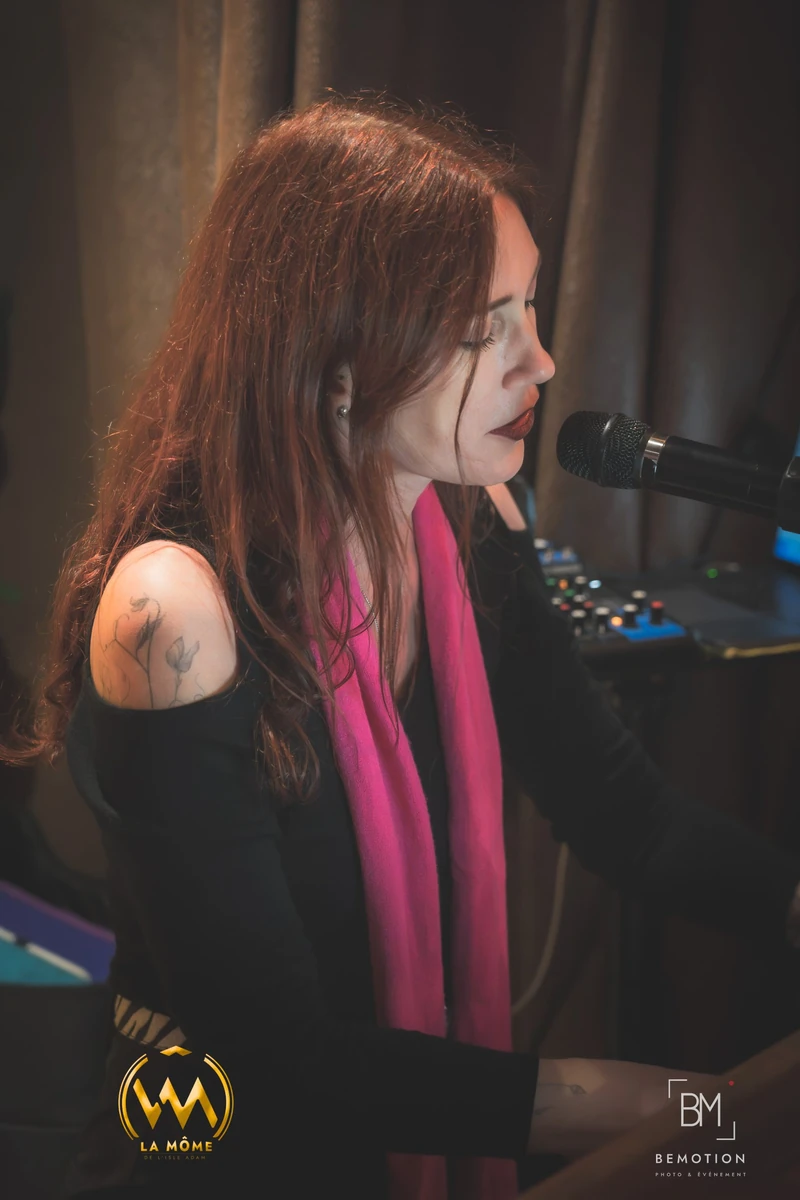 Portrait de Lollirox de profil, chantant au micro et jouant du piano, écharpe rose et cheveux roux