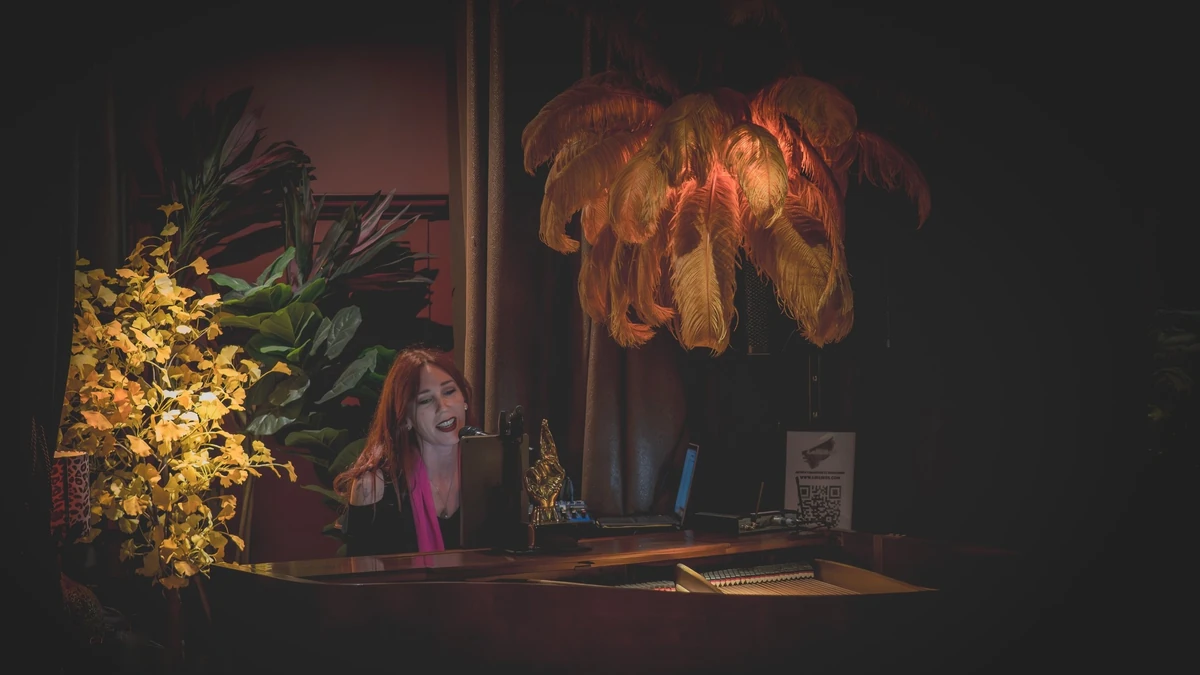 Lollirox chante au piano à queue, devant une grande lampe en plumes dorées, au restaurant La Môme à L’Isle-Adam
